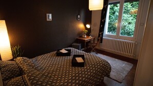 Ein Schlafzimmer mit zwei Betten, einem kleinen Tisch mit Lampe und einem Fenster mit Blick auf Grünflächen.