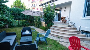 Eine Terrassenanlage mit Gartenmöbeln, einem roten Stuhl und einer Treppe, die zu einem Hauseingang führt.