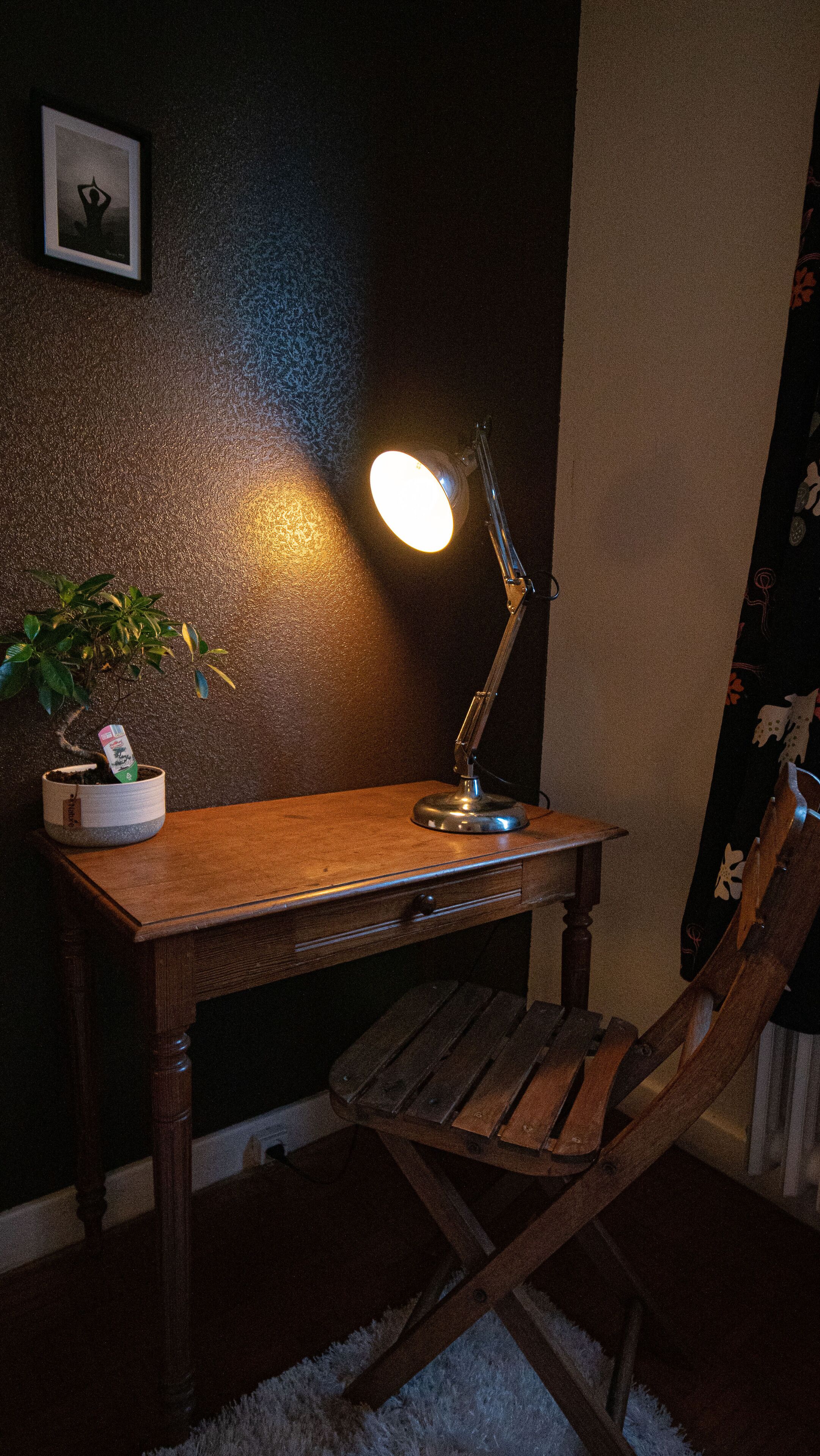 A wooden desk with a desk lamp, a potted plant, and a chair.