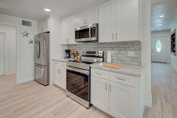 A modern kitchen with white cabinetry, stainless steel appliances, and a marble countertop. - Coastal Retreat (Nokomis)