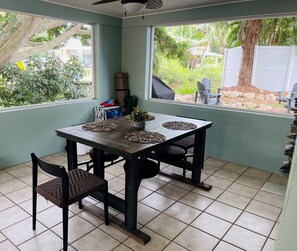A dining area with a table and chairs, a ceiling fan, and a view of greenery outside. - Coastal Retreat (Nokomis)