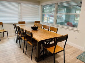 A dining area with a wooden table and chairs, a bowl of fruit, and a window with blinds. - Coastal Retreat (Nokomis)