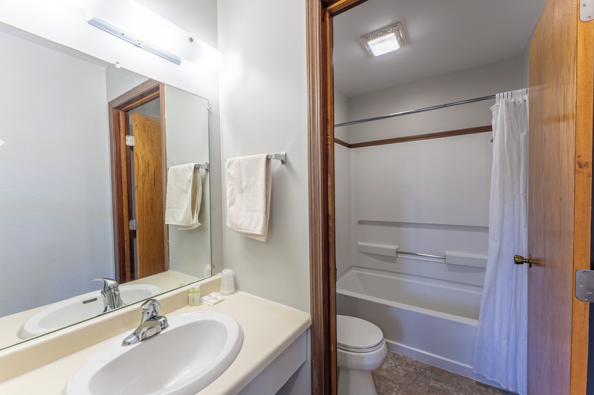 Baño con lavamanos, espejo, inodoro y zona de ducha.