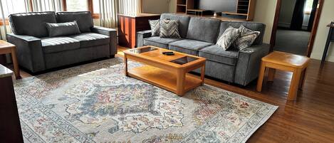 Una sala de estar con dos sofás grises, una mesa de centro de madera y una alfombra estampada.
