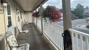 Une véranda couverte d’un motel, avec deux chaises, une rambarde et un jardinier.