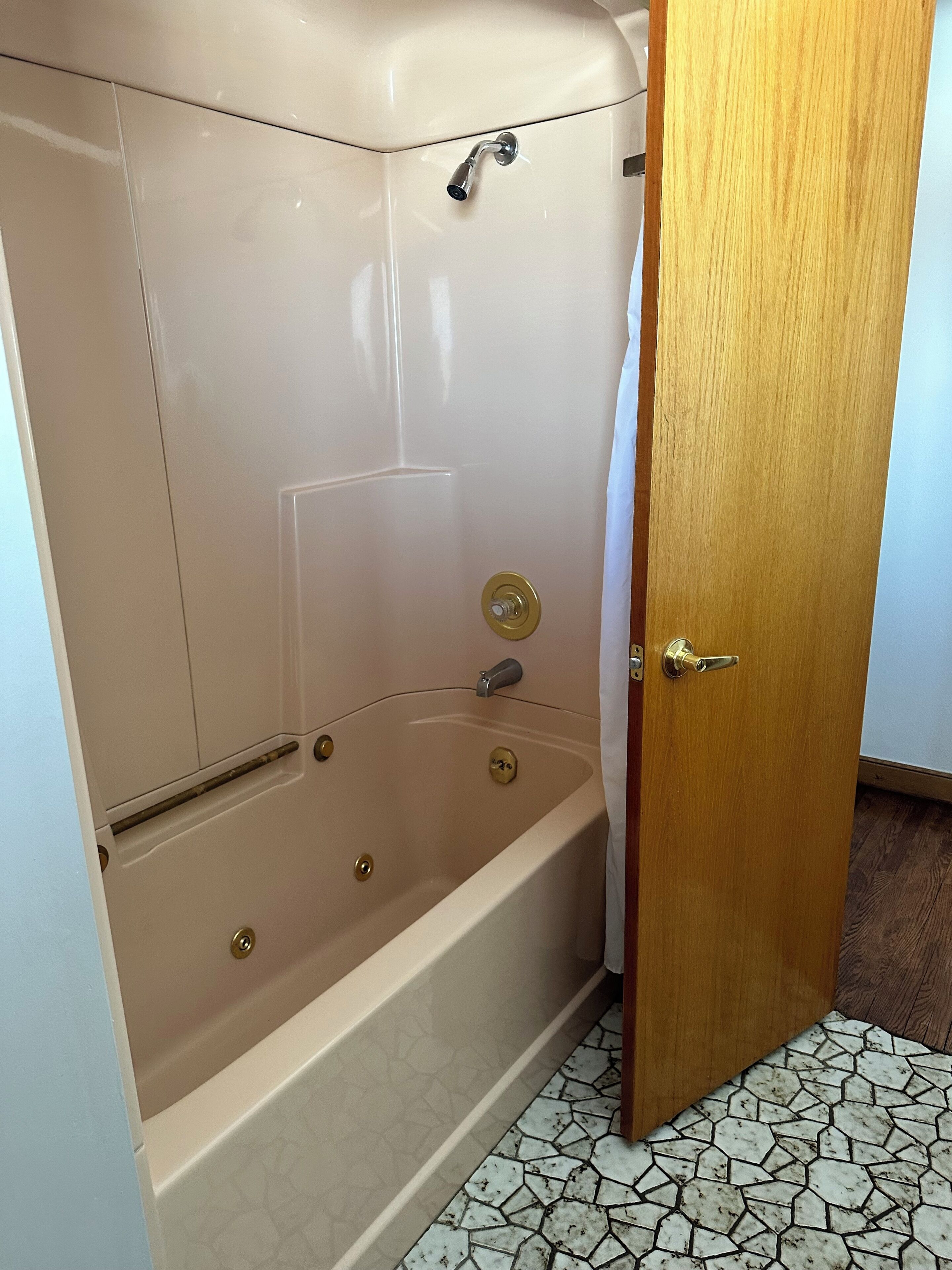 Une baignoire d’angle avec une porte en bois, une pomme de douche et un robinet.