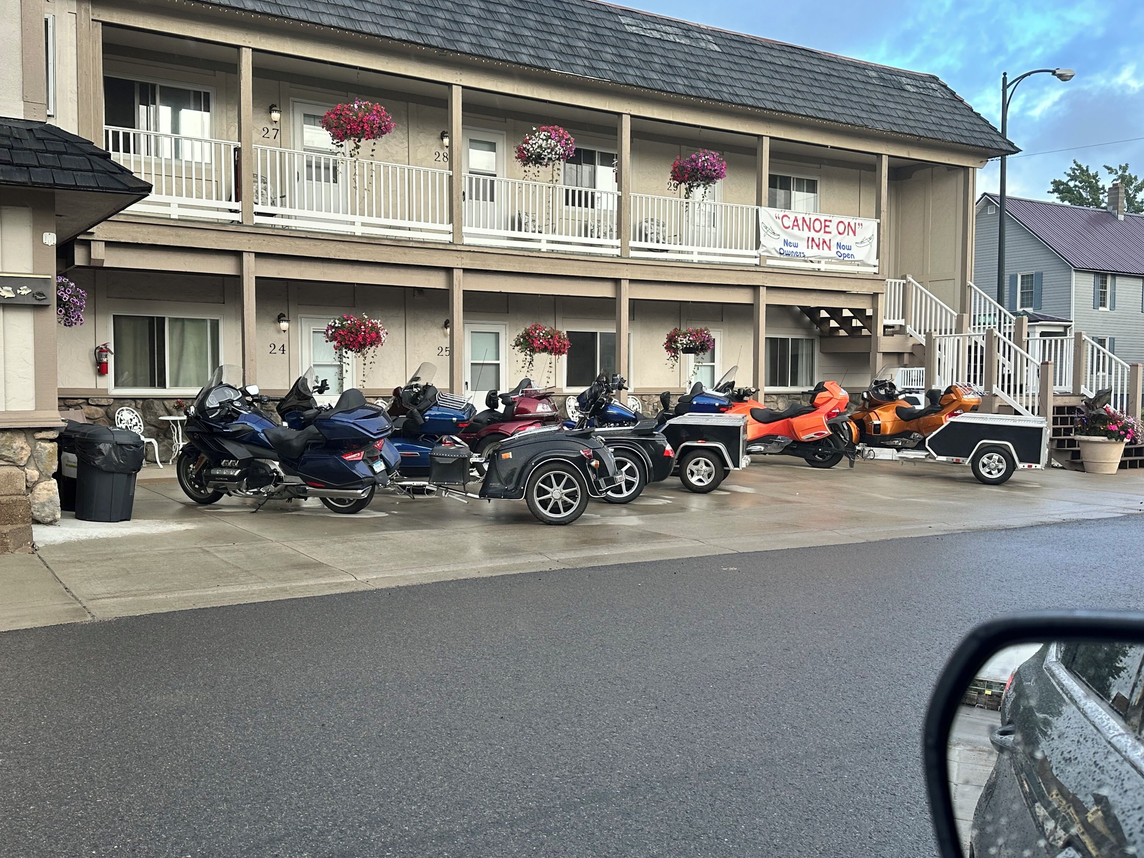 Un motel con una fila de motocicletas estacionadas frente, un letrero que anuncia alquiler de canoa y una jardinera en cada balcón.