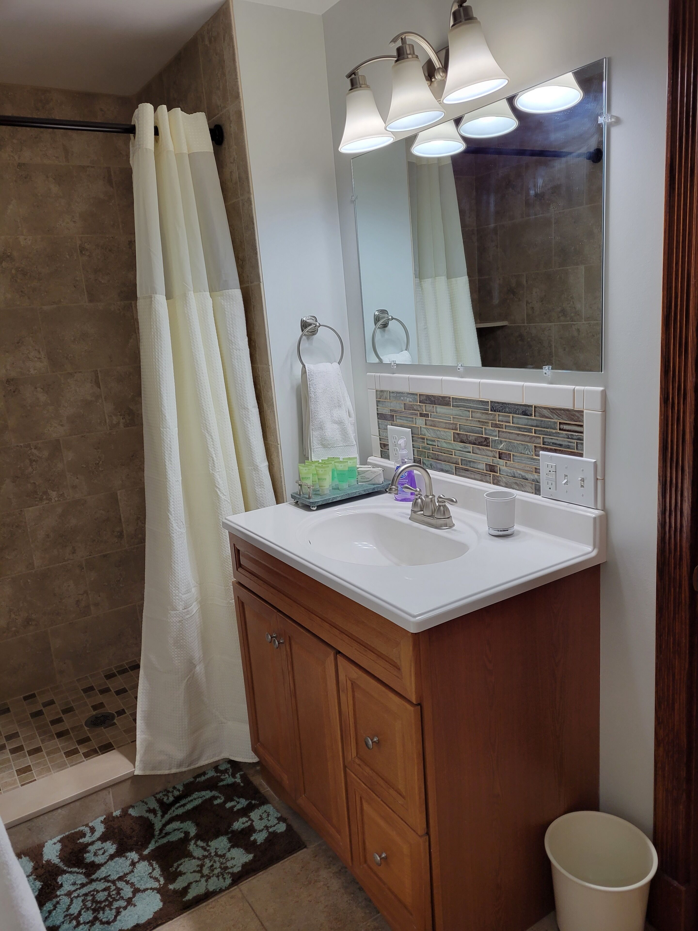 A bathroom with a shower, a sink with a mirror, and a wooden cabinet.