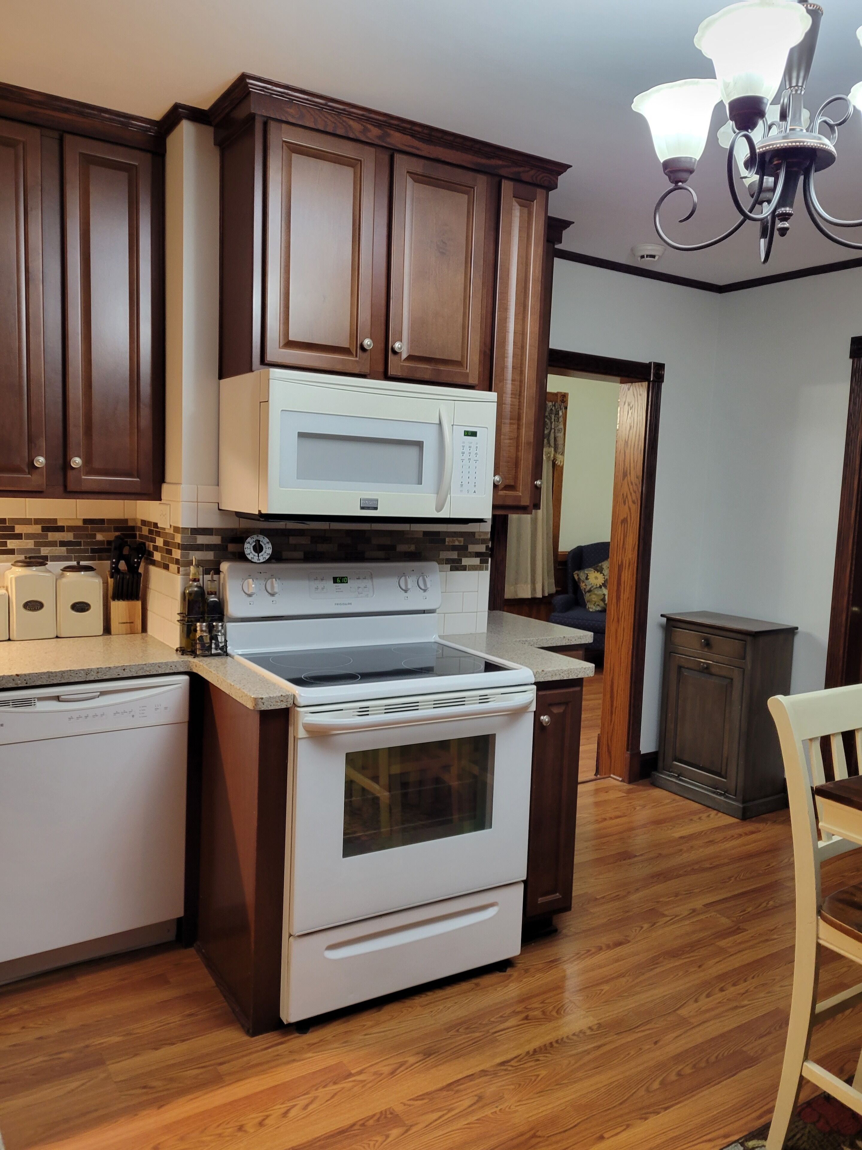 A kitchen with wooden cabinets, a white microwave, a stove, and a dishwasher.