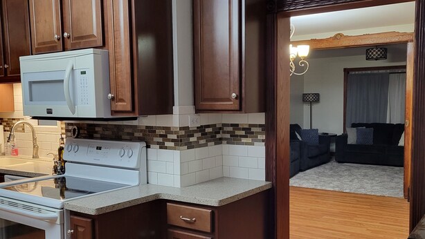 A kitchen with dark wooden cabinets, a white microwave, a stove, and a tiled backsplash.