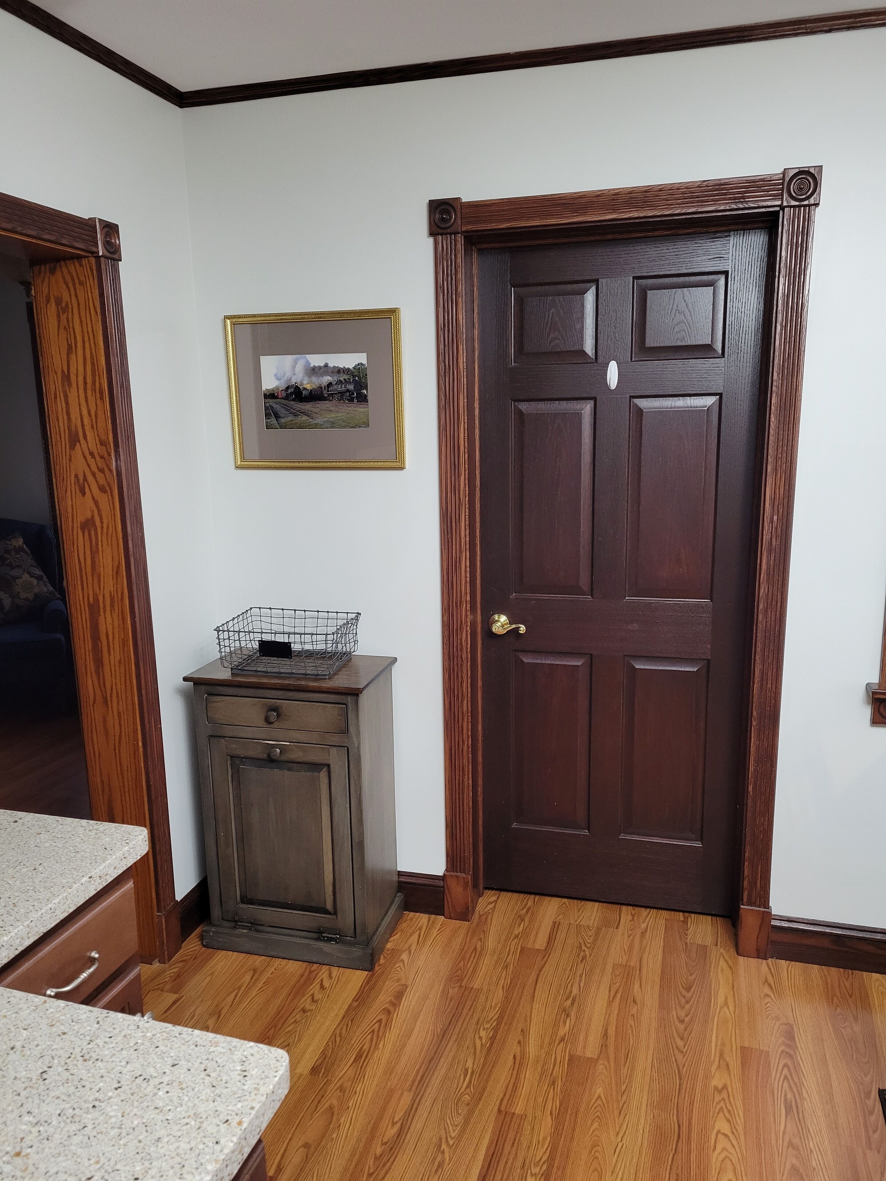 A room with a wooden door, a framed picture on the wall, a small cabinet, and a countertop.