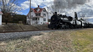 A steam locomotive on tracks with a house in the background.