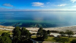 Un paisaje costero con vista despejada al mar, una playa arenosa y una zona verde con árboles.