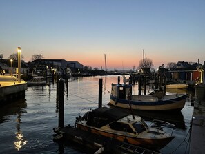 En småbåtshamn med förtöjda båtar, en brygga med folk som promenerar och byggnader i bakgrunden.