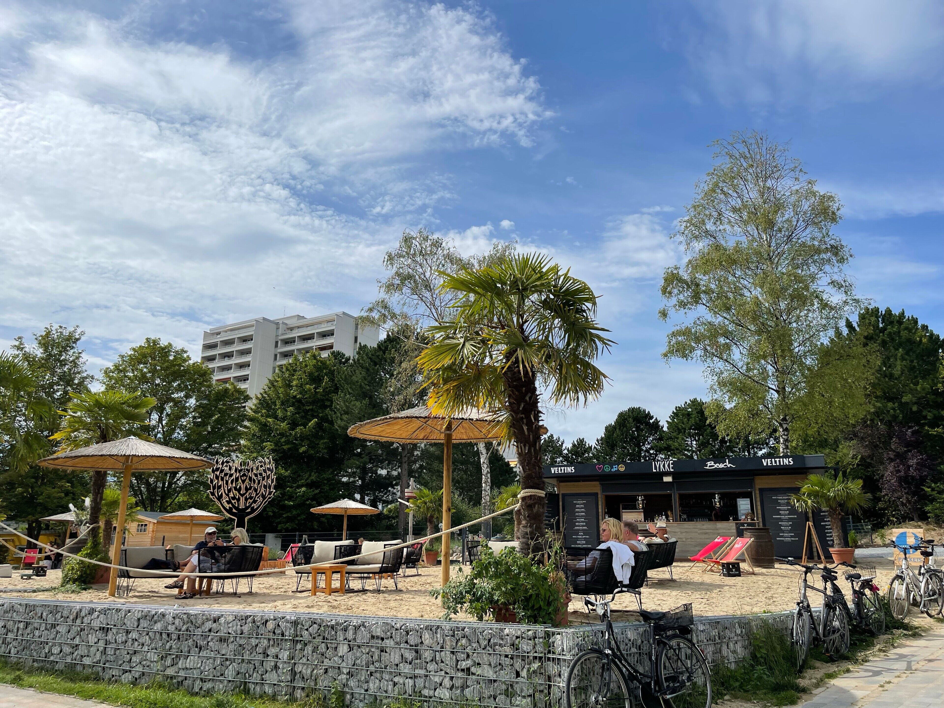 A beachside outdoor seating area with umbrellas, lounge chairs, and a stone wall.