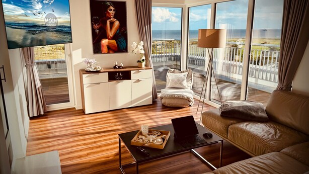 Una sala de estar moderna con un sofá, una mesa de centro, un televisor y un balcón con vista al mar.