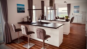 Una cocina moderna con una isla central, taburetes de bar, una cafetera y vistas al exterior.