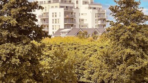 Un edificio residencial de varios pisos con balcones, rodeado de abundante vegetación y una masa de agua.