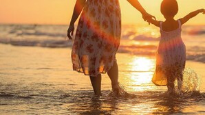 Atardecer sobre el océano con dos personas tomadas de la mano.