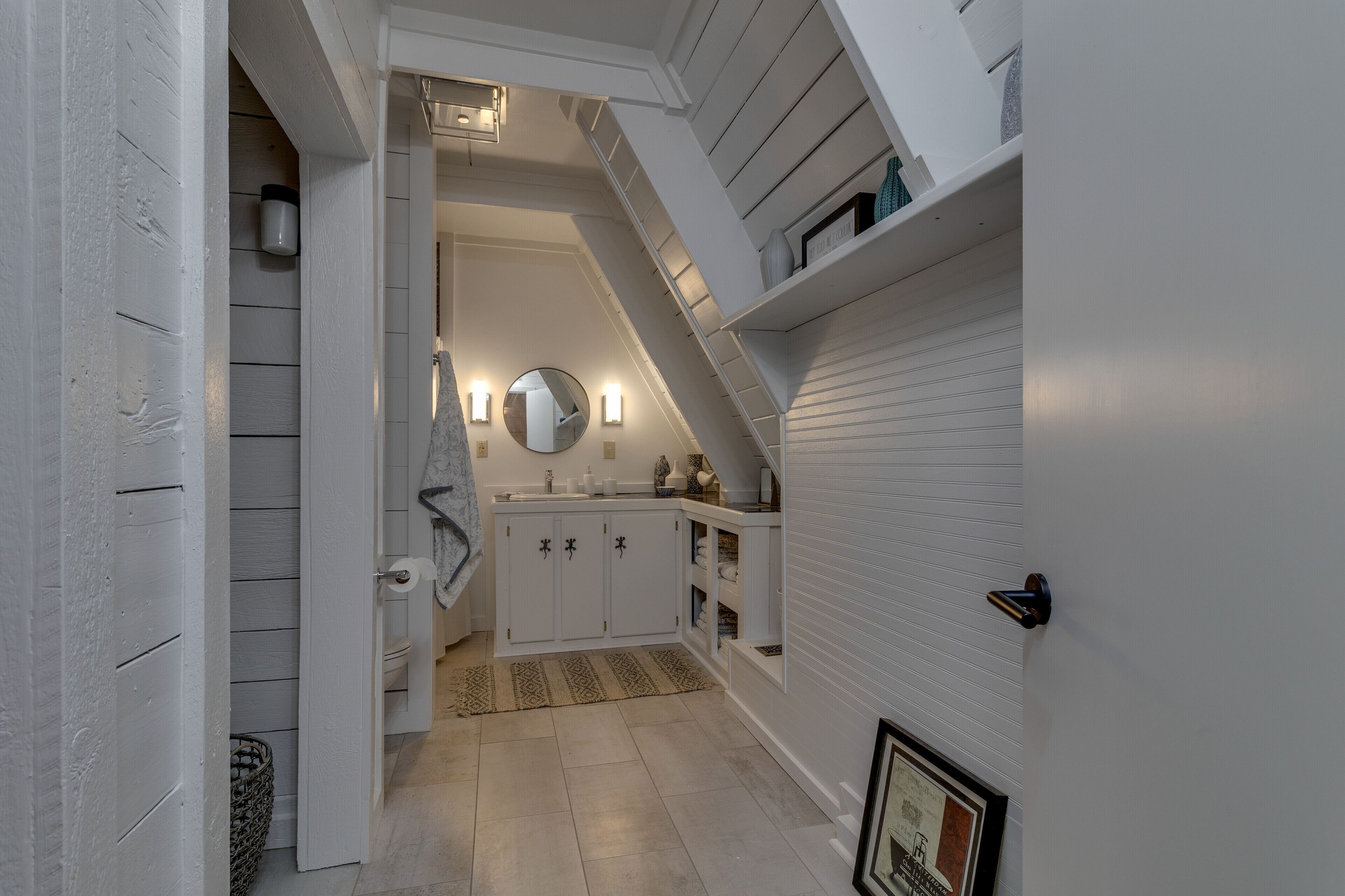 Un couloir étroit avec un escalier menant à un deuxième étage. Les murs sont blancs, et il y a un petit coin cuisine avec des placards et un évier.