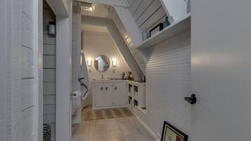 Un couloir étroit avec un escalier menant à un deuxième étage. Les murs sont blancs, et il y a un petit coin cuisine avec des placards et un évier.