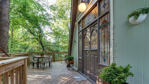 Un patio in legno con tavolo e sedie, immerso nel verde.