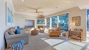 A spacious living room with a fireplace, large windows, and a ceiling fan. - Seaflower Cove: Spacious 4bd Oceanfront Retreat (Gualala)