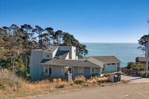 A coastal house with a garage, a small porch, and a view of the ocean. - Seaflower Cove: Spacious 4bd Oceanfront Retreat (Gualala)