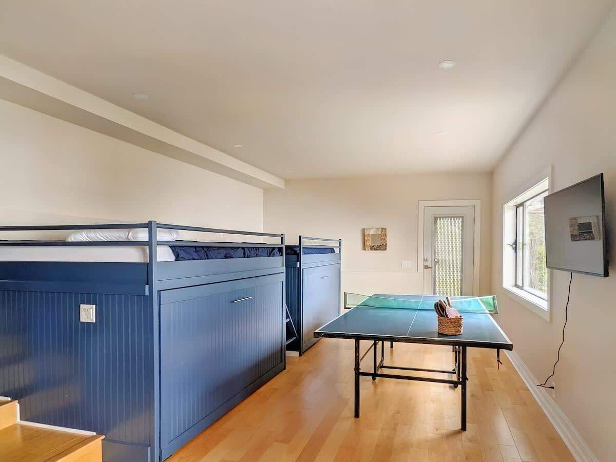 A room with bunk beds, a ping pong table, and a TV mounted on the wall.