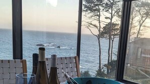A table with a meal, wine bottles, and a view of the sea. - Seaflower Cove: Spacious 4bd Oceanfront Retreat (Gualala)