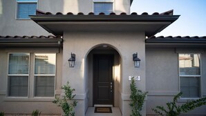 A two-story house with a dark front door, two windows with shutters, and a small welcome mat.