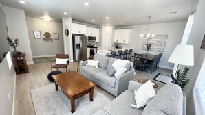 A modern living room with a grey sofa, wooden coffee table, and a dining area with a chandelier.