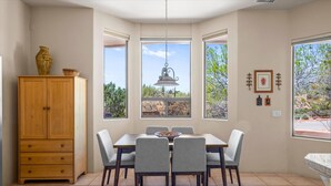 A dining area with a wooden cabinet, a table with chairs, and large windows offering a view of the outdoors. - Luxury Sedona Retreat • Hot Tub & Fire Pit (Sedona)