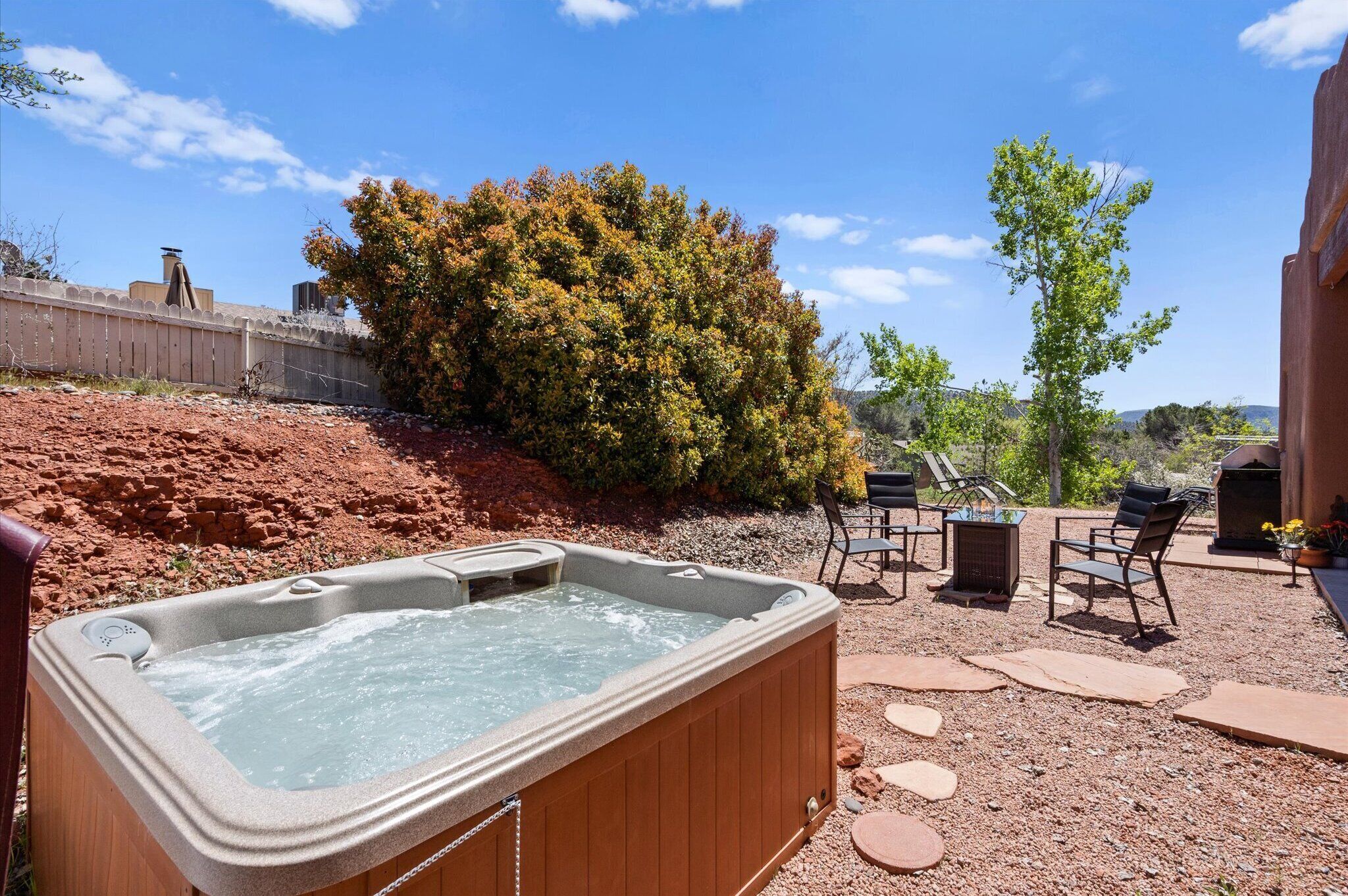 Un jacuzzi en un patio trasero con zona de terraza, mobiliario exterior y un árbol grande.