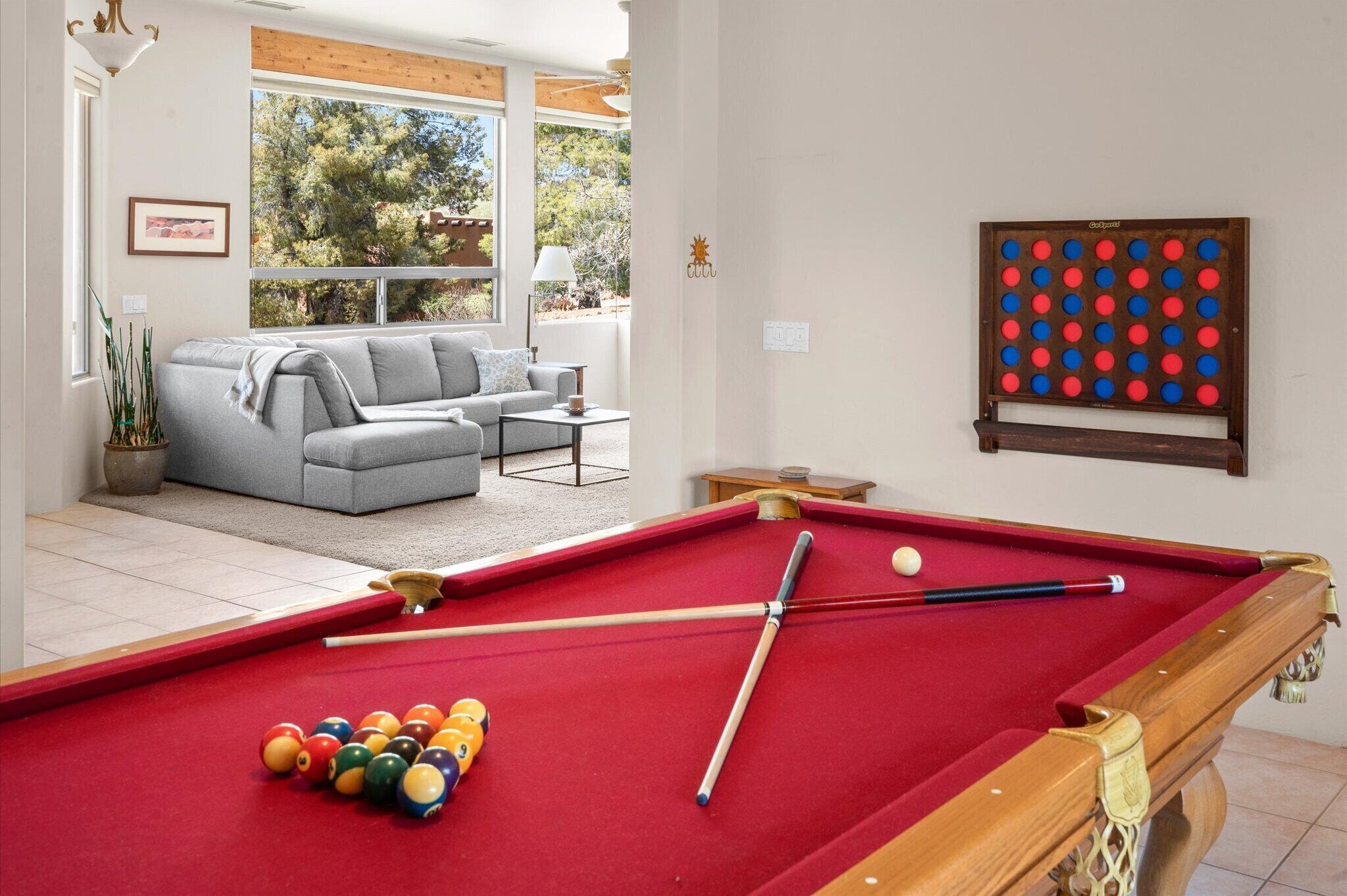 A pool table with balls, a sofa, and a table lamp in a room with a window and a wooden ceiling.