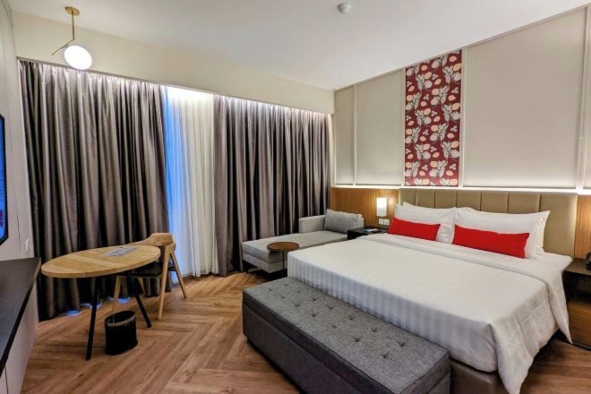 A hotel room with a large bed, a sofa, a small table, and a bench.