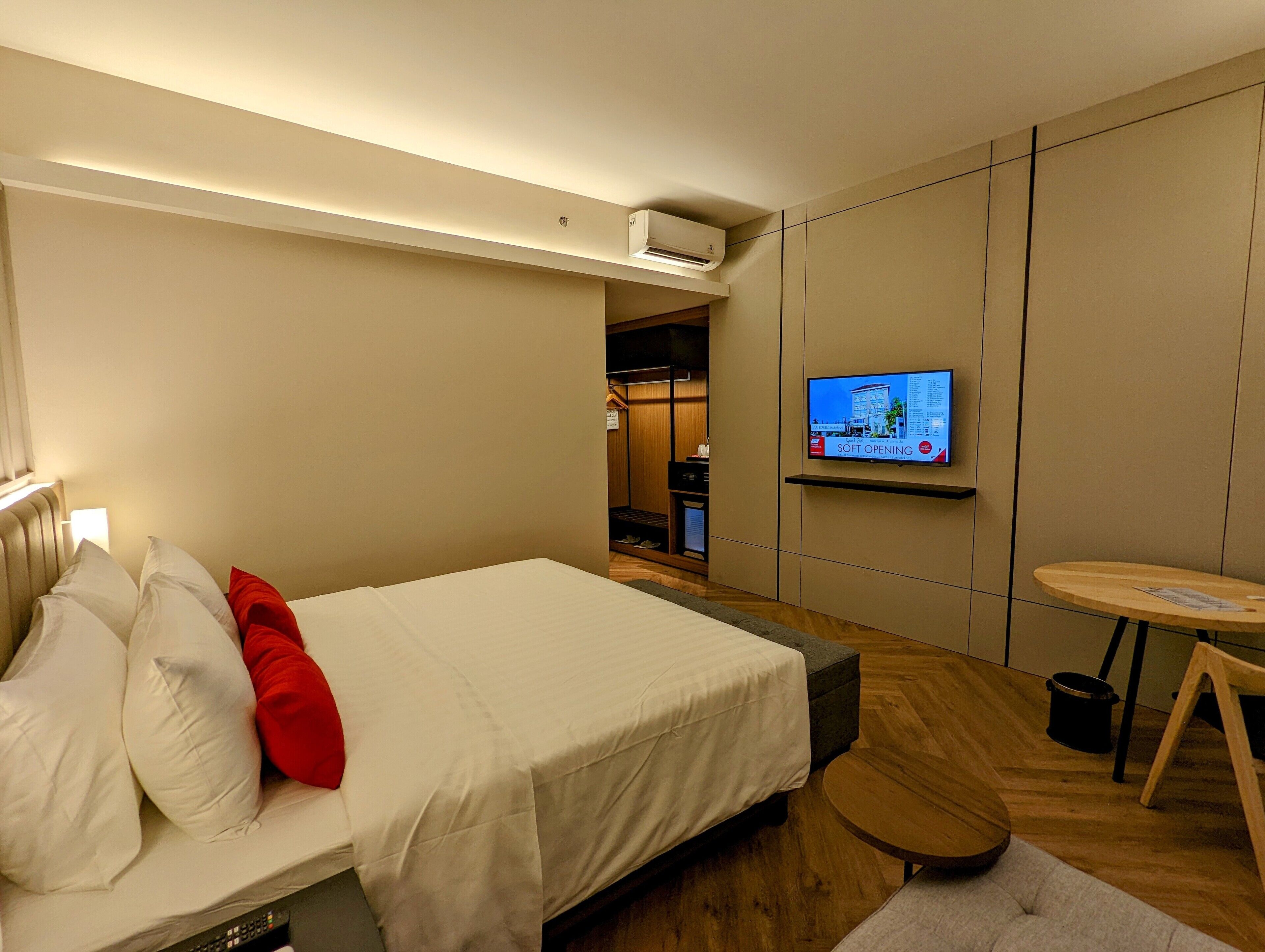 Habitación de hotel con cama, televisor montado en la pared, una mesita redonda y suelo de madera.