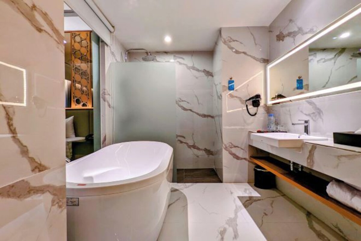 A modern bathroom with a freestanding bathtub, a vanity with a mirror, and marble-patterned walls.