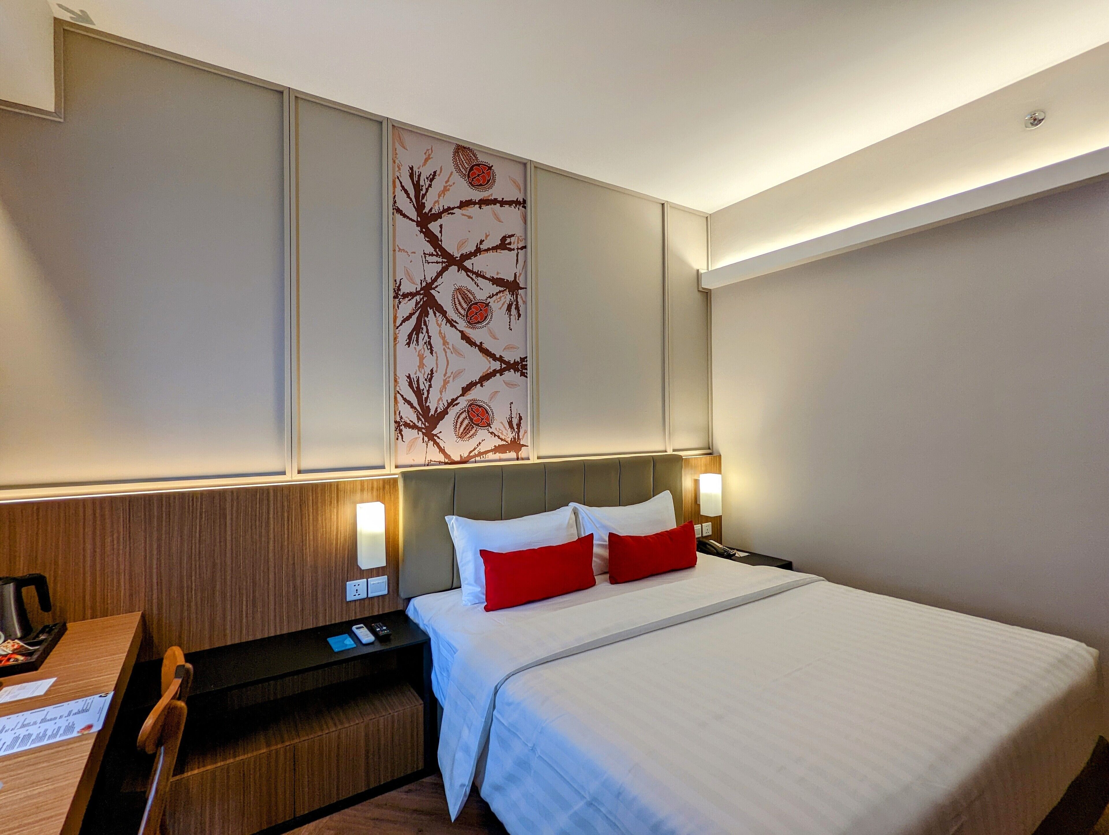 Una habitación de hotel con cama, mesita de noche, lámpara y un panel decorativo en la pared.