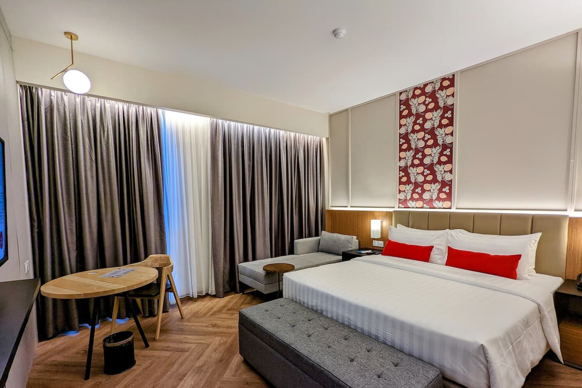 Une chambre d’hôtel avec un grand lit, un bureau, une chaise, une petite table et un banc.