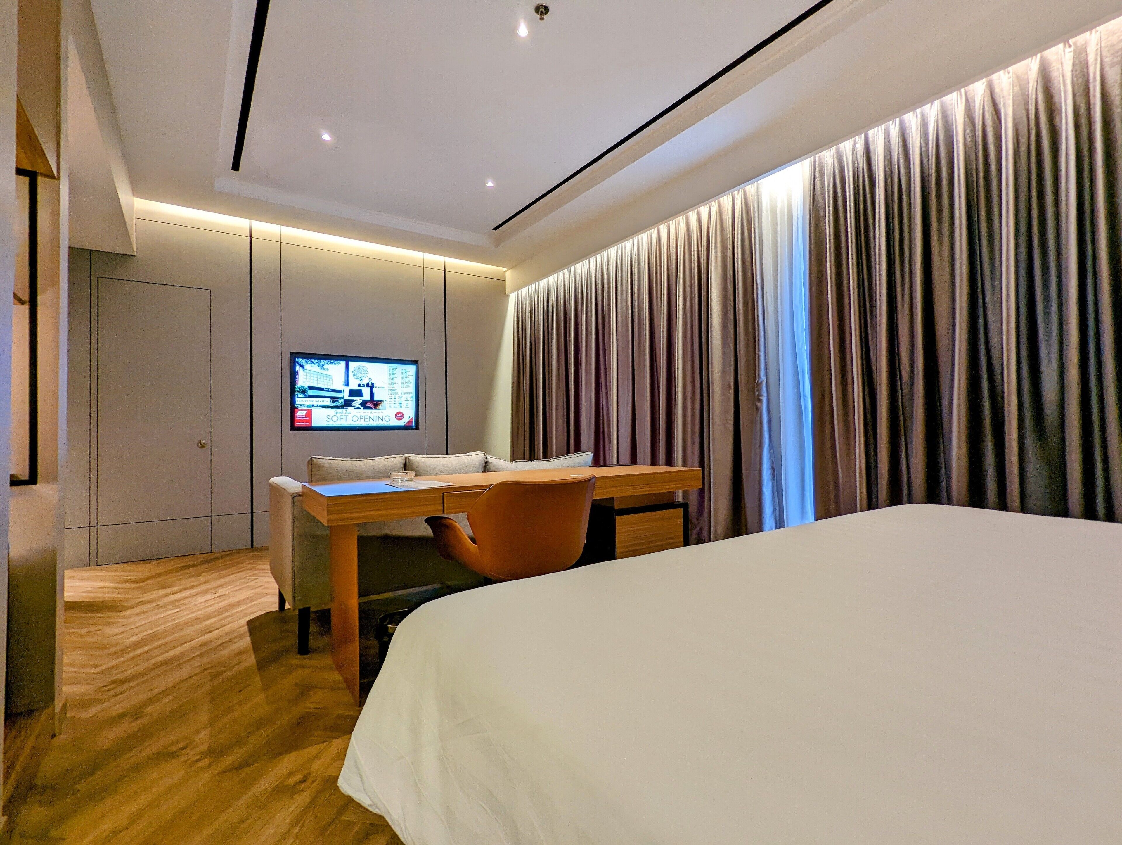 A modern hotel room with a large bed, a wooden desk, a comfortable chair, and a television on the wall.