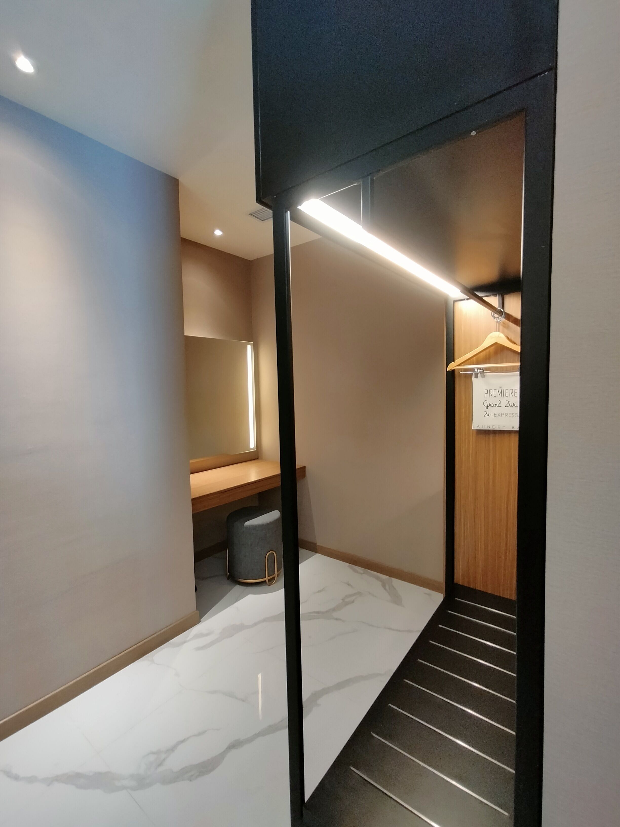 Un couloir d’hôtel moderne avec un sol en marbre, un banc en bois, un porte-manteau suspendu et un panneau indiquant qu’un événement spécial est prévu.