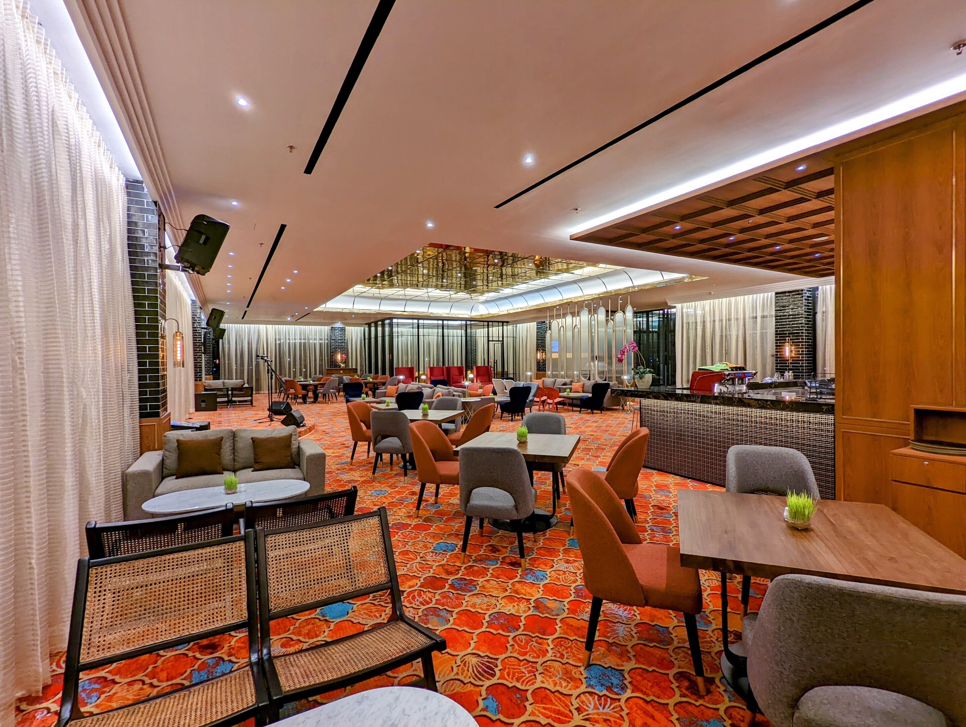 A spacious hotel lobby with a central seating area, multiple tables, and a bar.