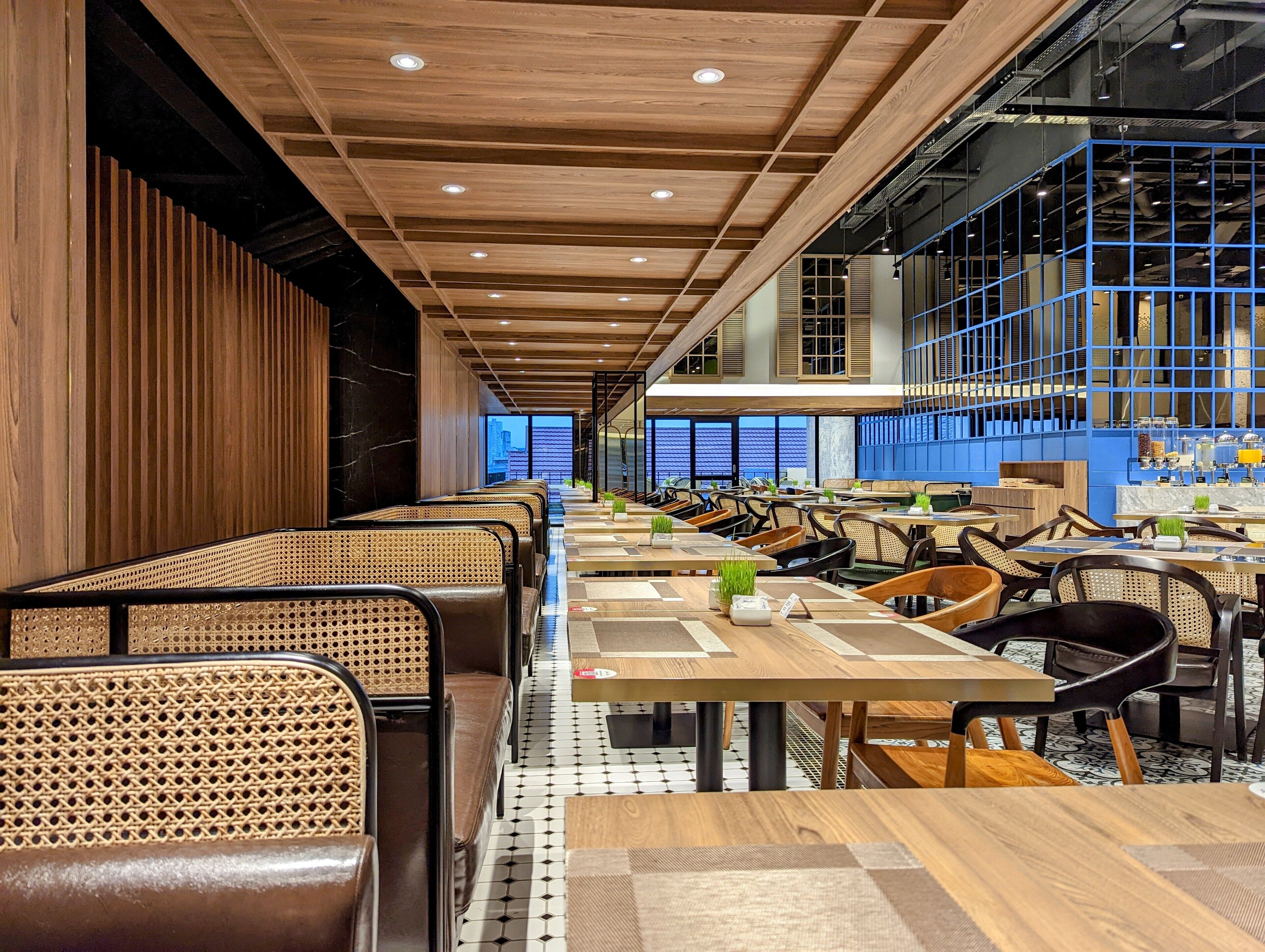 A modern restaurant interior with wooden ceiling beams, black leather seating, and a tiled floor.