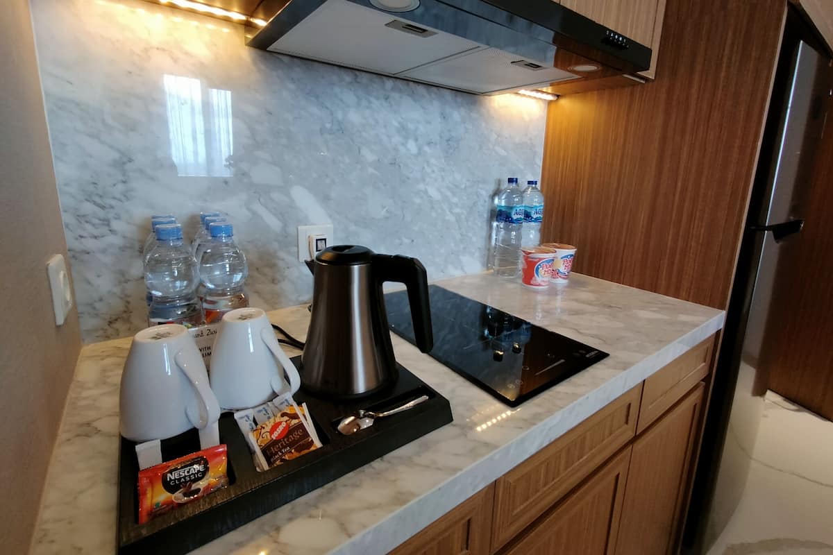 Une cuisine moderne dotée d’une hotte en acier inoxydable, de plans de travail en marbre et de meubles en bois. On y trouve des bouteilles d’eau, une bouilloire et une machine à café sur le plan de travail.
