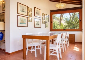Un coin repas avec une table en bois et des chaises blanches, agrémenté d’œuvres d’art sur le thème maritime, encadrées et disposées le long du mur.
