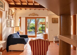 Un salon comprenant un canapé, un fauteuil à rayures, une table et une vue sur un jardin, visible à travers une porte vitrée.