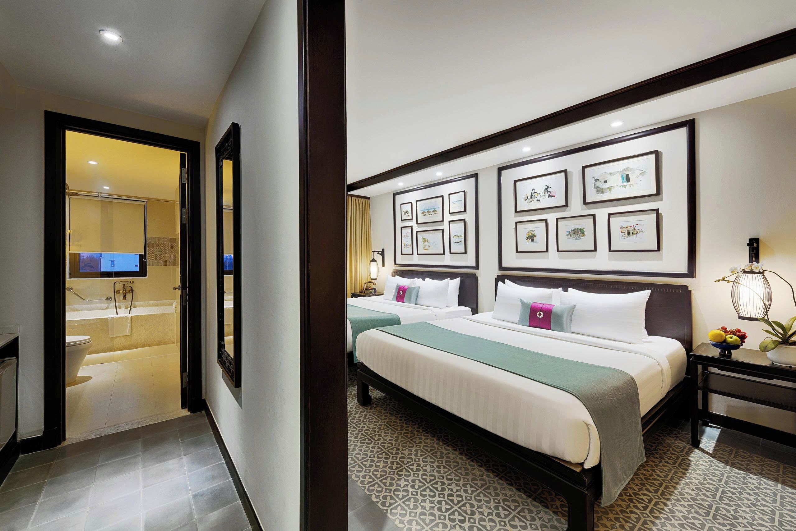 A hotel room with two beds, a bathroom, and a hallway leading to a bathroom.