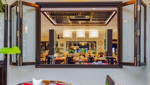 A dining area with a large mirror reflecting the interior, wooden ceiling with a grid pattern, and a table set with a red napkin and white napkin holder. - Wyndham Garden Hoi An Cua Dai Beach (Da Nang)