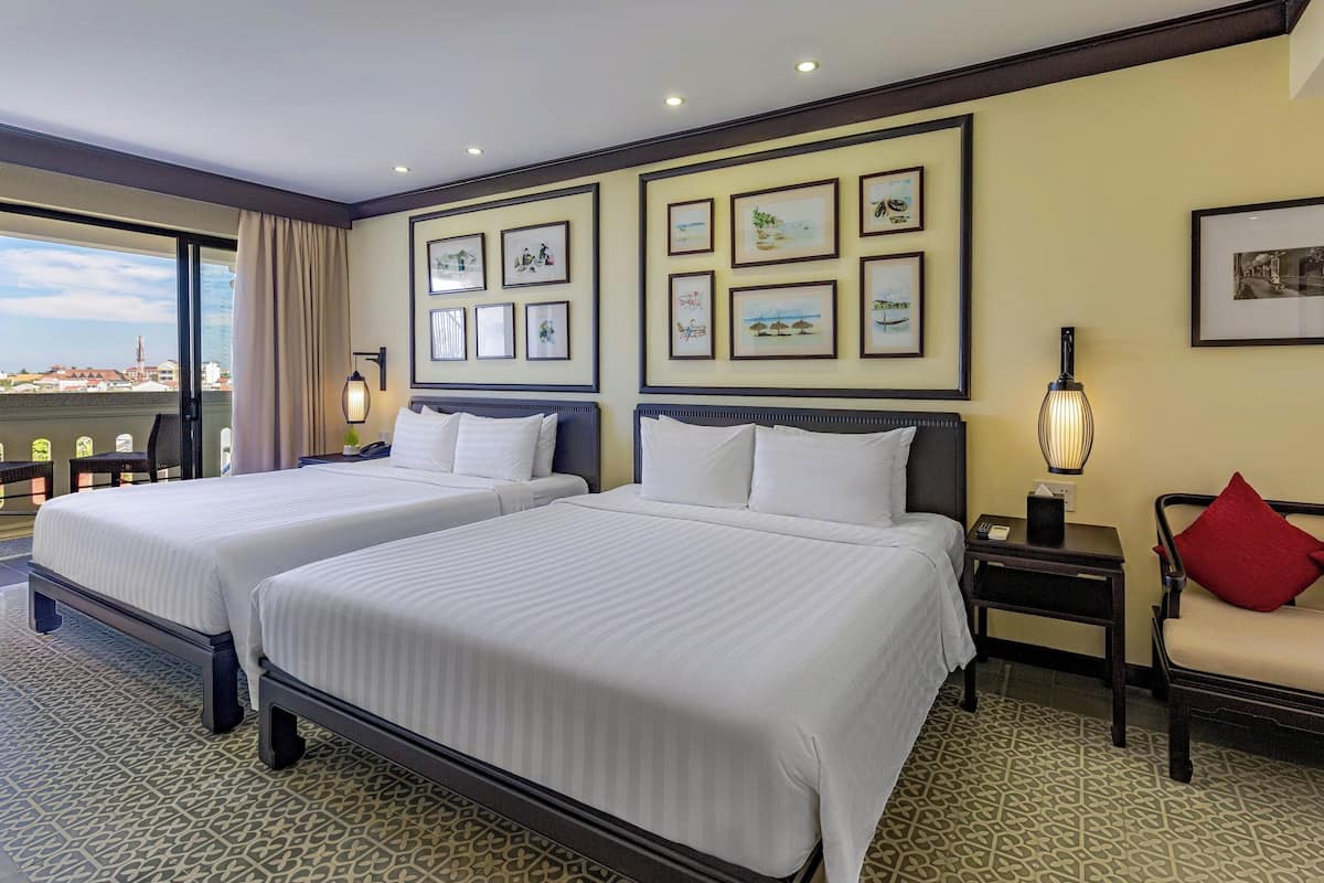 A hotel room with two beds, a large window with a view, and several framed pictures on the wall.